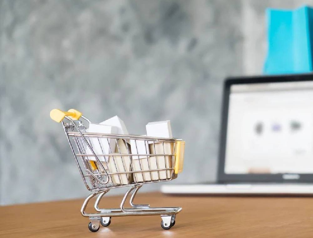 A tiny shopping cart parked beside a laptop